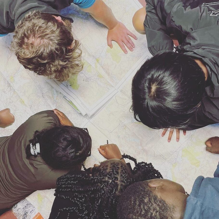 A group of cadets gathered around a large map, studying routes and planning navigation during a training or expedition activity. 
